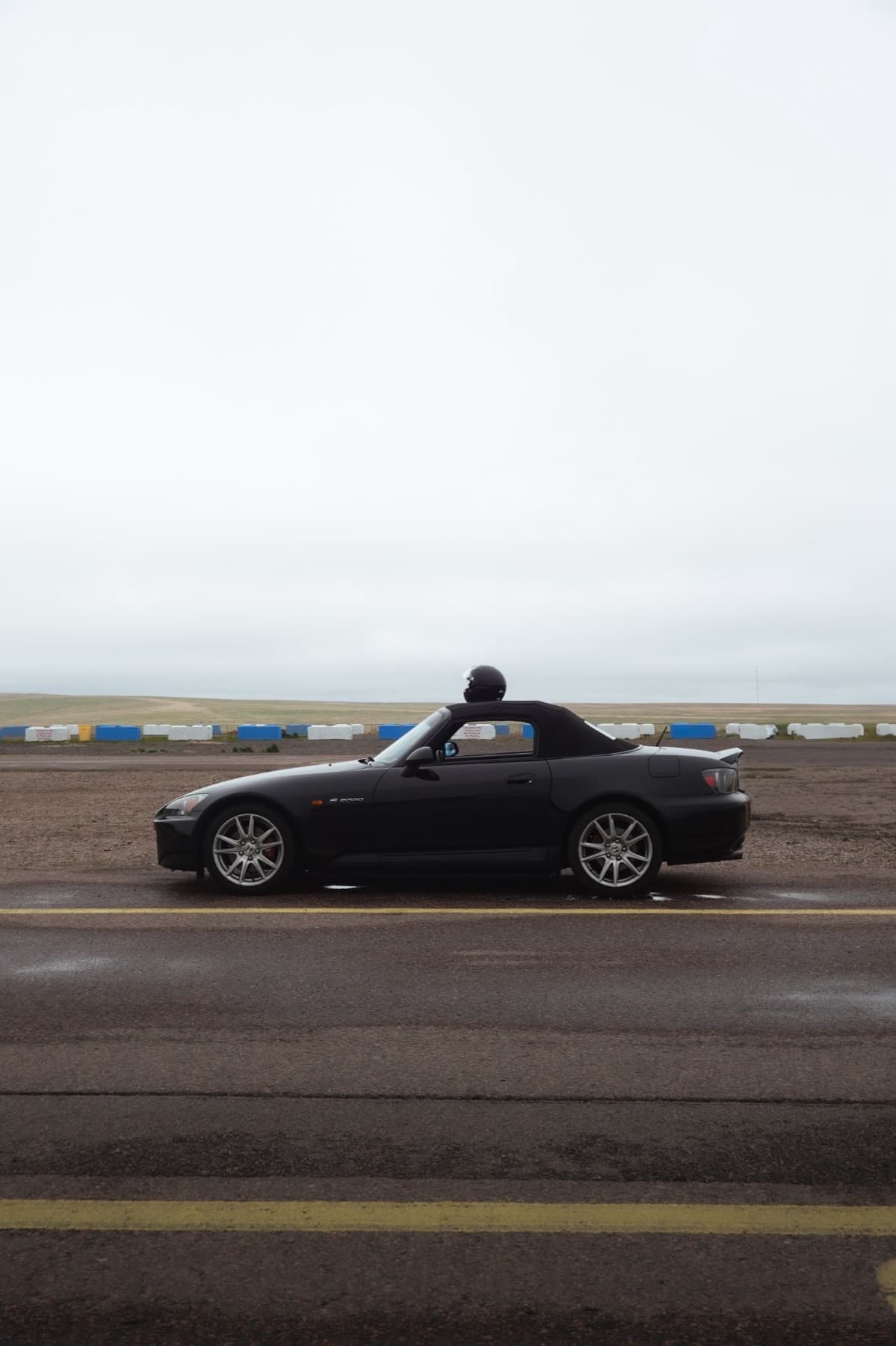 Black Honda S2000 with a helmet on the roof at a racetrack